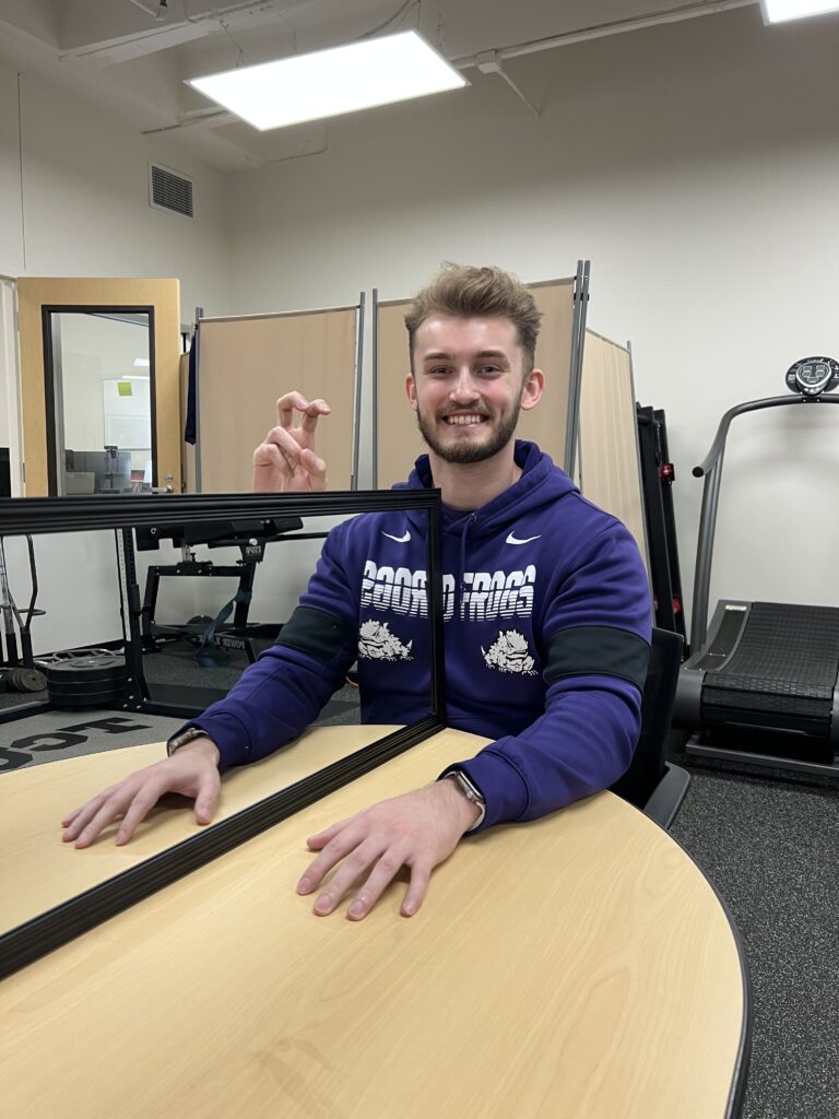 Voskuil with his arm on a table and a mirror reflecting it, conducting an experiment